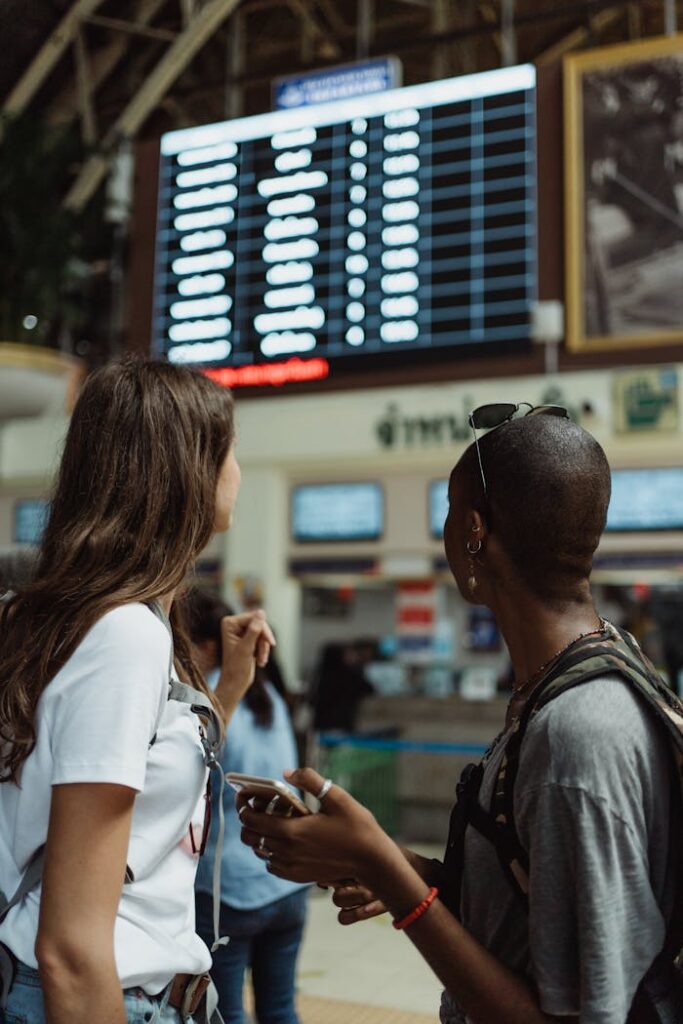 Two women checking the flight schedule on a departure board in an airport terminal, preparing for travel.
